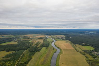 Bulutlu bir yaz gününde nehir, tarla ve çam ormanlarının üzerinden uçmak