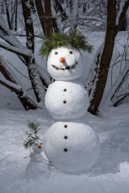 İki kardan adam, büyük ve küçük havuç burun, karlı kış parkında şapka ve düğmeler.