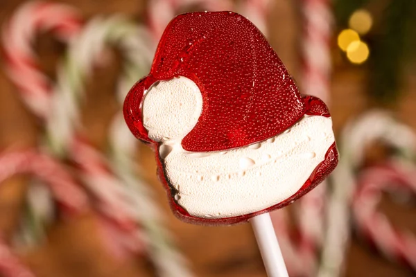 Christmas candy caramel red hat on sticks in close-up on a background of caramel canes — Stock Photo, Image