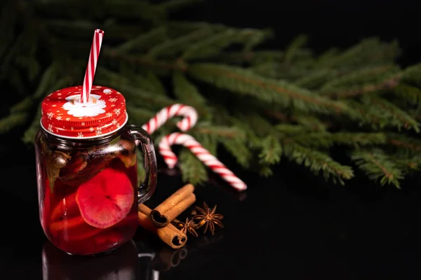 レモンとスパイスのクリスマスカクテルシナモンと星のアニスは、キャンディー杖を持つクリスマスツリーの黒の背景にあります。 — ストック写真