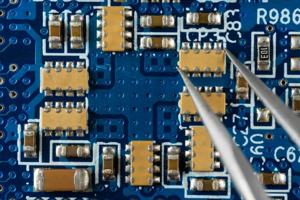 Instalación o eliminación de componentes electrónicos en una placa electrónica azul con pinzas, soldadura —  Fotos de Stock
