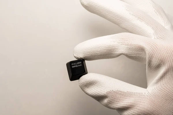 Una mano en un guante blanco sostiene un botón de teclado negro con una inscripción Pausa Break blanca sobre un fondo blanco — Foto de Stock