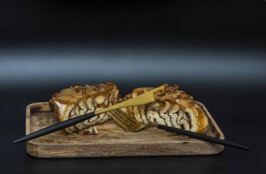 Kesik tarçınlı rulo ekmeğin kenarına karamelli ve fındıklı, tahta tepside, siyah bir arka planda çatal ve bıçakla...