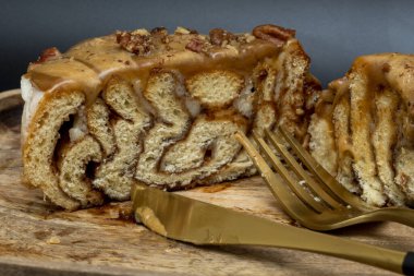 Kesik tarçınlı rulo ekmeğin kenarına karamelli ve fındıklı, tahta tepside, siyah bir arka planda çatal ve bıçakla...