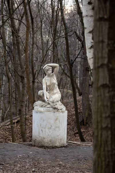 Statue of a seated half-naked woman in a park in spring