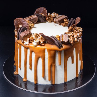 Siyah arka planda patlamış mısır ve kurabiyeli beyaz pasta, yakın plan.