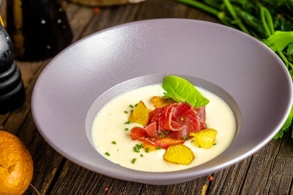 Rustic wooden background, top and side, on a plate, white cream soup of smoked potato, with beef jerky, herbs and vegetables — Stock Image Rustic Wooden Background Top Side Plate White Cream Soup Smoked Stock Photo