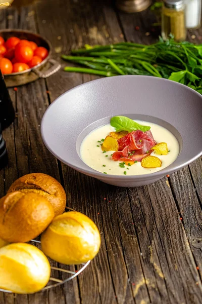 Rustic wooden background, top and side, on a plate, white cream soup of smoked potato, with beef jerky, herbs and vegetables — Stock Image Rustic Wooden Background Top Side Plate White Cream Soup Smoked Stock Picture