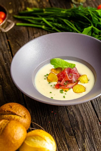 Rustic wooden background, top and side, on a plate, white cream soup of smoked potato, with beef jerky, herbs and vegetables — Stock Image Rustic Wooden Background Top Side Plate White Cream Soup Smoked Royalty Free Stock Images