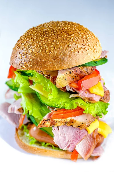 big sandwich or rustic burger, meat with white bread or a bun, two sausages, smoked delicacies, salad, tomato, lettuce, vegetables, cheese, on a white isolated background
