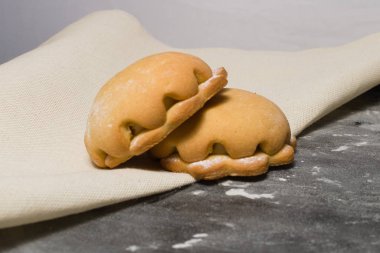 Dalgalı bir kenarla pişirmek ve doğal kumaştan yapılmış bir peçeteye un serpiştirilmiş siyah bir masanın üzerinde duruyor. Çay için tatlı çörekler..