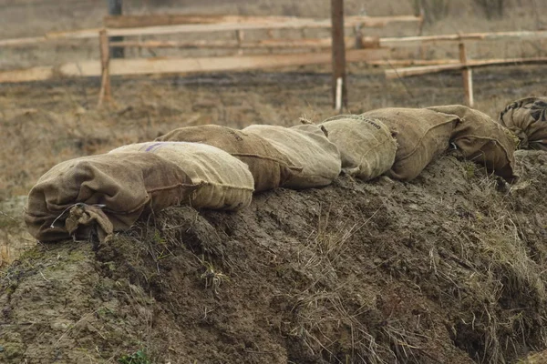 Sandbags feitos de tecido grosso reforçam a borda da trincheira do exército no campo. Preparar posições de infantaria durante exercícios. — Fotografia de Stock