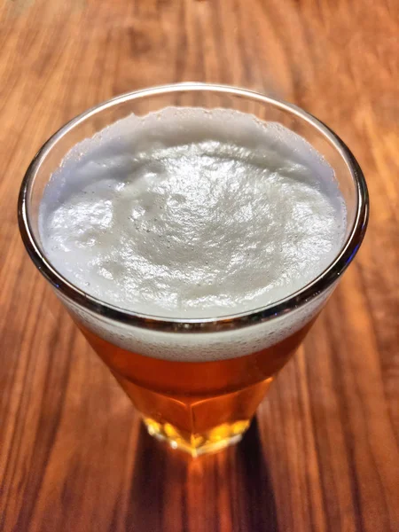 Vidrio con cerveza ligera con hacer espuma en una mesa de madera en una orientación vertical del marco — Foto de Stock