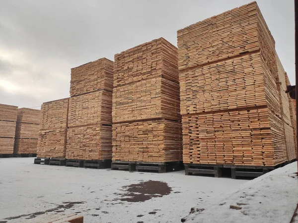Φυσικές ξύλινες σανίδες στοιβαγμένες σε μια στοίβα σε μια ανοιχτή αποθήκη ξυλείας στο χιόνι Εικόνα Αρχείου
