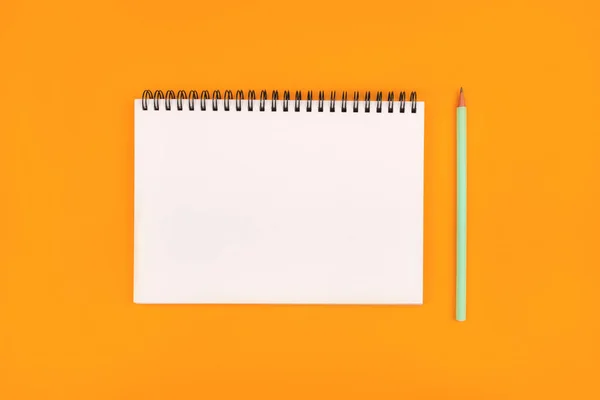 オレンジの背景に空のノートと鉛筆、トップビュー. — ストック写真
