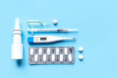 Mavi arka planda dijital termometre ve ilaçlar.