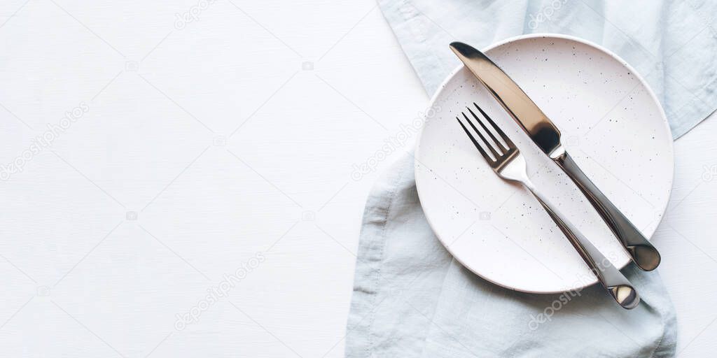 An empty plate and Cutlery on a white table.