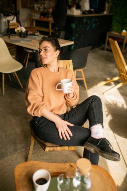 Kafede otururken dizüstü bilgisayarla iş yapan genç bir kadının portresi..