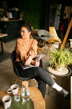 Kafede otururken dizüstü bilgisayarla iş yapan genç bir kadının portresi..