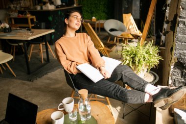 Kafede otururken dizüstü bilgisayarla iş yapan genç bir kadının portresi..