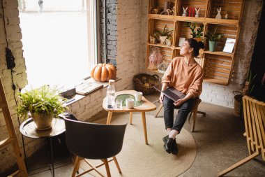 Kafede otururken dizüstü bilgisayarla iş yapan genç bir kadının portresi..