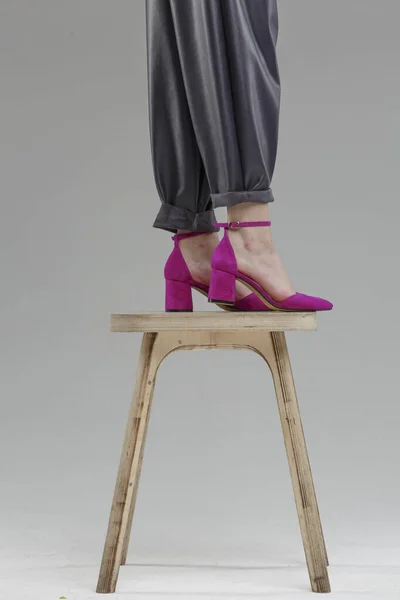 Legs in shoes of beautiful young woman standing on chair against plain wall, no brand, copy space