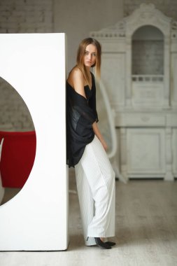 Beyaz kutu geometrik stüdyo arka planında oturan çizgili ve siyah bluzlu moda görünümlü kız, süpermodel pozu, ayakta ve oturma pozları fotokopi alanı