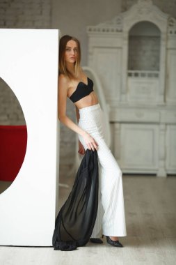 Beyaz kutu geometrik stüdyo arka planında oturan çizgili ve siyah bluzlu moda görünümlü kız, süpermodel pozu, ayakta ve oturma pozları fotokopi alanı