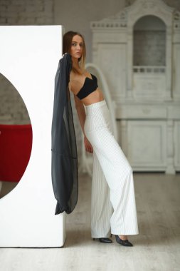 Beyaz kutu geometrik stüdyo arka planında oturan çizgili ve siyah bluzlu moda görünümlü kız, süpermodel pozu, ayakta ve oturma pozları fotokopi alanı