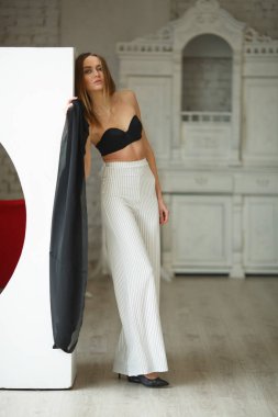 Beyaz kutu geometrik stüdyo arka planında oturan çizgili ve siyah bluzlu moda görünümlü kız, süpermodel pozu, ayakta ve oturma pozları fotokopi alanı