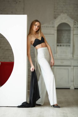 Beyaz kutu geometrik stüdyo arka planında oturan çizgili ve siyah bluzlu moda görünümlü kız, süpermodel pozu, ayakta ve oturma pozları fotokopi alanı
