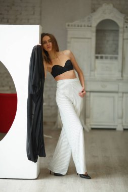 Beyaz kutu geometrik stüdyo arka planında oturan çizgili ve siyah bluzlu moda görünümlü kız, süpermodel pozu, ayakta ve oturma pozları fotokopi alanı