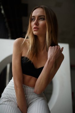 Beyaz kutu geometrik stüdyo arka planında oturan çizgili ve siyah bluzlu moda görünümlü kız, süpermodel pozu, ayakta ve oturma pozları fotokopi alanı