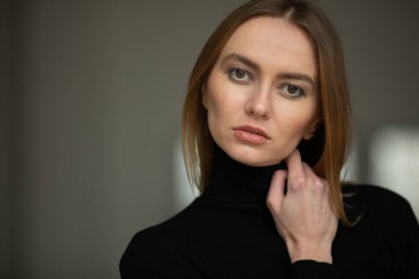 Siyah balıkçı yaka yakalı, mavi gözlü, iç mekanda poz veren, stüdyo geçmişi olan şık görünümlü bir kızın portresi. 