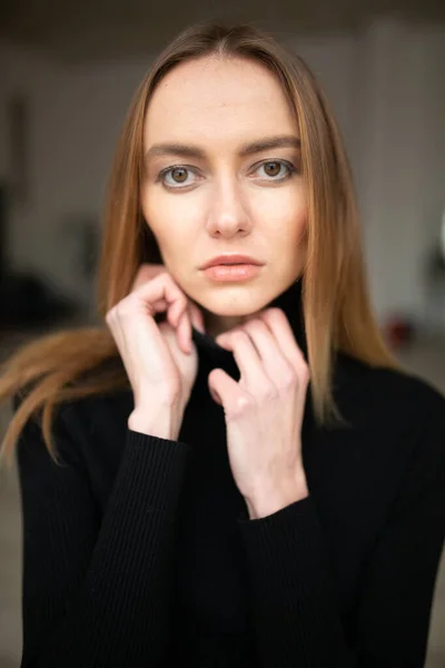 close up portrait of stylish looking girl in black turtleneck with blue eyes, model posing in interior, studio background