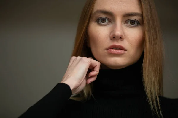 close up portrait of stylish looking girl in black turtleneck with blue eyes, model posing in interior, studio background