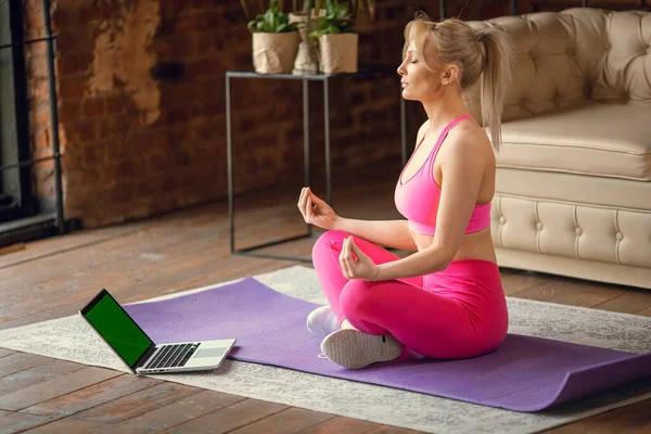 Closeup young sporty fit slim woman coach do practice video online training yoga instructor modern laptop meditate,  relax breathe easy seat pose gym healthy lifestyle concept.Sport at home
