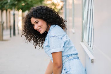 Genç, kıvırcık bir kızın, duvara yaslanmış gülümseyen portresini yakından çek.