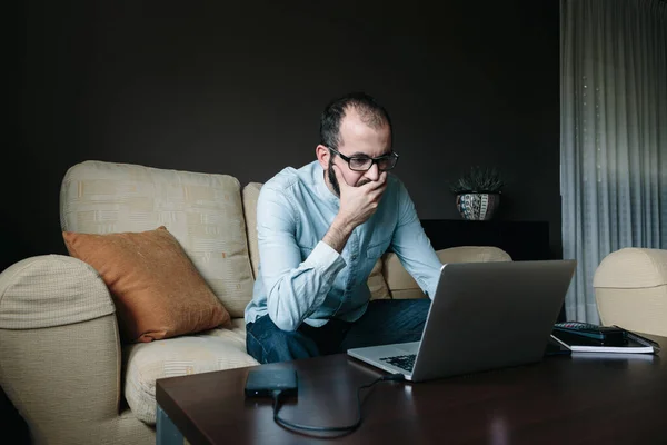 Worried man reading the news on the laptop computer while working remotely from his living room at home