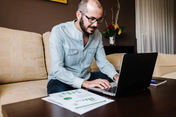 Man working on laptop from home and analyzing financial data with graphics and charts. Finance economic and business impact crisis by coronavirus