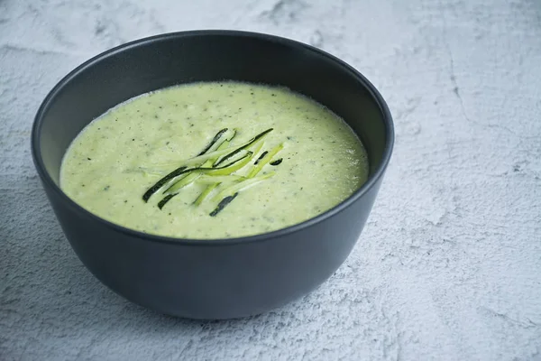 stock image Cream soup made from mashed potatoes with zucchini and basil and crackers on a light background. Space for text.