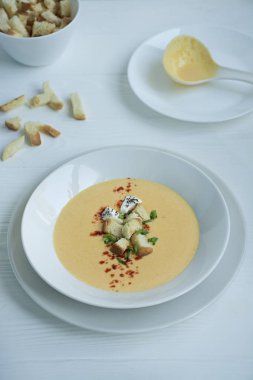 Peynir çorbası, kraker, otlar ve peynir. Krema çorbası beyaz tabakta servis edilir. Beyaz arkaplan.