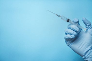 Mavi eldivenli bir elin elinde şırınga var. Doktor aşı için bir şırınga tutuyor. İlaçlar. Mavi arkaplan, mesaj için yer. Boşluğu kopyala.