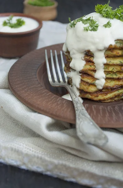 Zucchini fritters. Vegetarian zucchini pancakes served with fresh herbs and sour cream. A stack of pancakes. Light background.