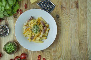 Peynirli İtalyan makarnası, balkabağı ve kızarmış domuz pastırması, beyaz tabakta servis ediliyor. Hafif ahşap zemin. Metin için boşluk.