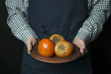 Aşçı elinde bir hurma tutuyordu. Erkek eli taze hurma dolu bir tabak tutar. Mevsimlik meyveler. Koyu arkaplan.