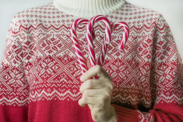 身穿圣诞毛衣的女孩在白色背景上拿着圣诞糖果手杖，特写。 圣诞节的背景 案文的篇幅. — 图库照片