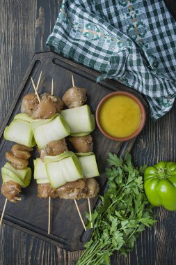 Bir kesme tahtası üzerinde sos, sebze ve otlar ile kabak ile bir şiş üzerinde Şişler. Koyu ahşap arka plan.