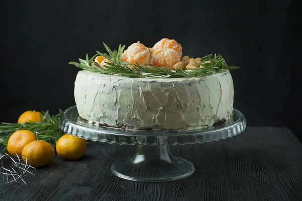 Pastel de Navidad con mandarinas, almendras y romero en un soporte. Pastel de Navidad con crema batida. Fondo oscuro. Espacio para texto . — Foto de Stock