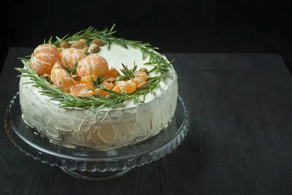 Christmas cake with tangerines, almonds and rosemary on a stand. Christmas cake with whipped cream. Dark background. Space for text. — Stock Photo, Image